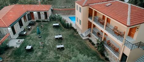 A two-story building with a red-tiled roof, a swimming pool, and outdoor seating areas.