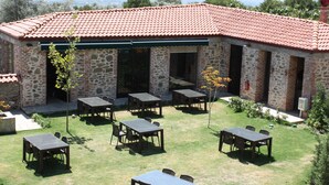 Un edificio de piedra con techo de tejas, zona de estar al aire libre con mesas y sillas, y un césped.