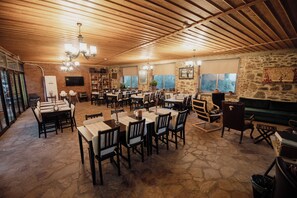 A spacious indoor dining area with stone flooring, wooden ceiling beams, and multiple tables and chairs. - Rukim Otel (Odemis)