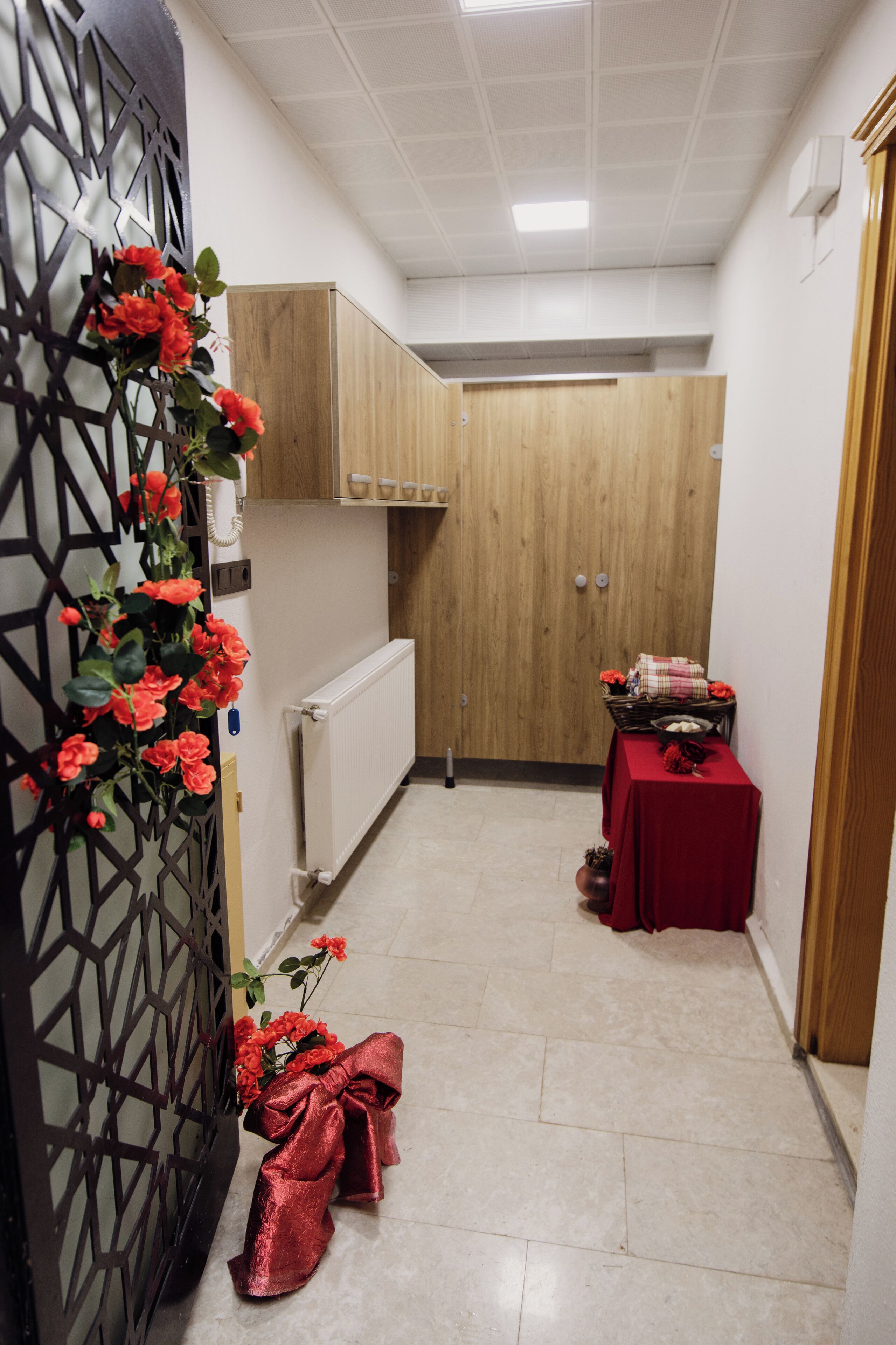 A narrow hallway with a radiator, a wooden door, and a table with a red tablecloth.