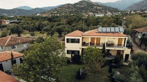 Un edificio de dos pisos con balcón, rodeado de árboles y vistas a un paisaje montañoso.