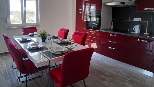 A modern kitchen with red cabinets, a dining table with red chairs, and a pendant light. - Ivan's holiday home (Zemunik Donji)