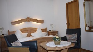 A cozy room with a wooden headboard, a bed with white pillows, a small table with a basket, and two chairs. - Pension Allebrodt (Lennestadt)