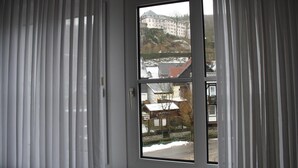 A room with a large window offering a view of a building with a snow-covered roof and a fence. - Pension Allebrodt (Lennestadt)
