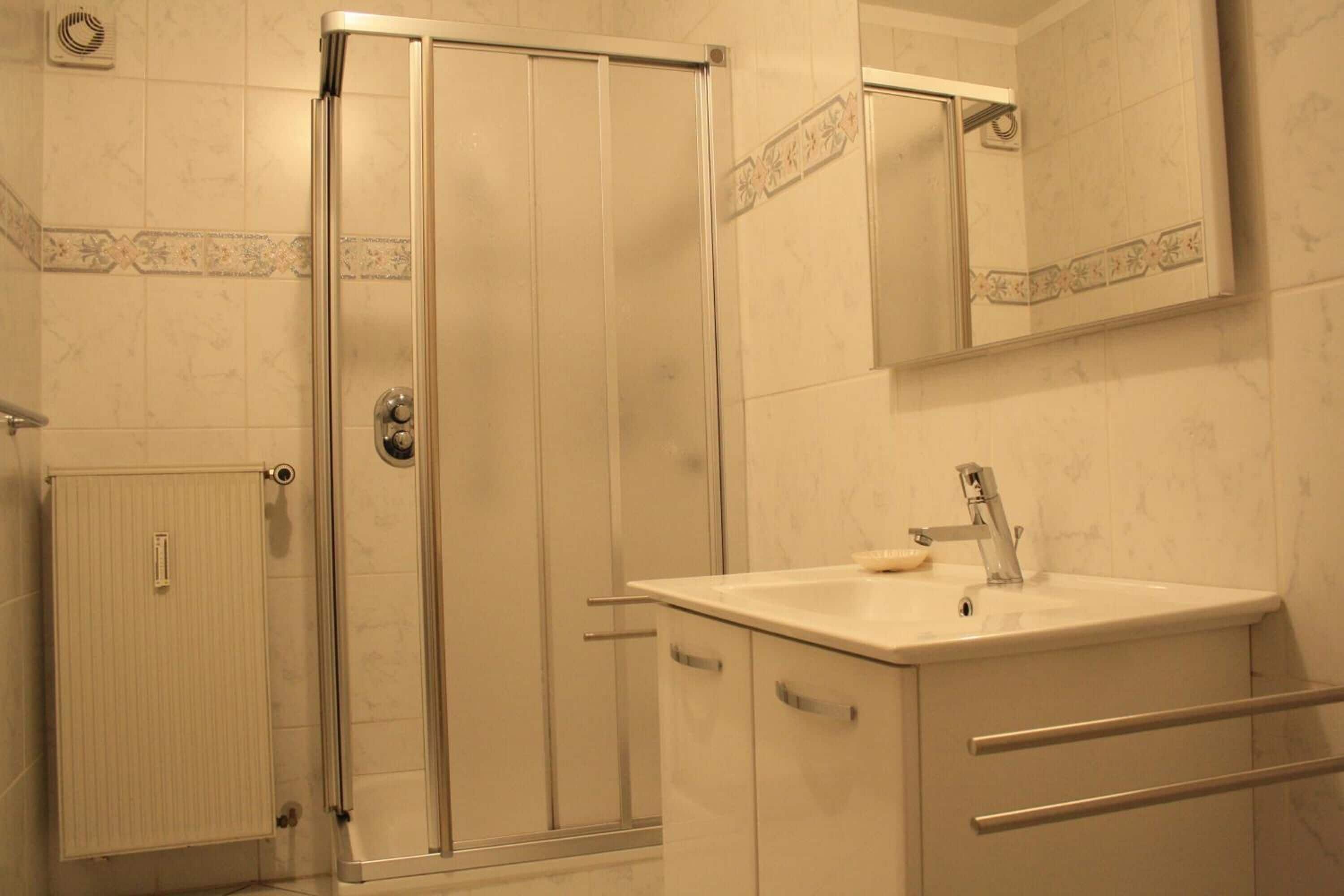 Un bagno con box doccia in vetro, lavandino con specchio sopra e termosifone.
