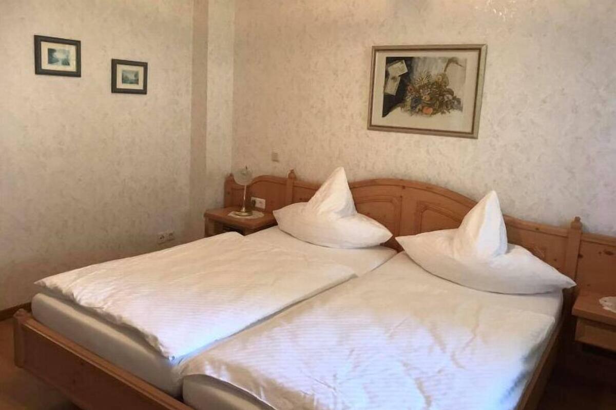 A double bed with white bedding and two pillows, a wooden headboard, a nightstand with a lamp, and two framed pictures on the wall.