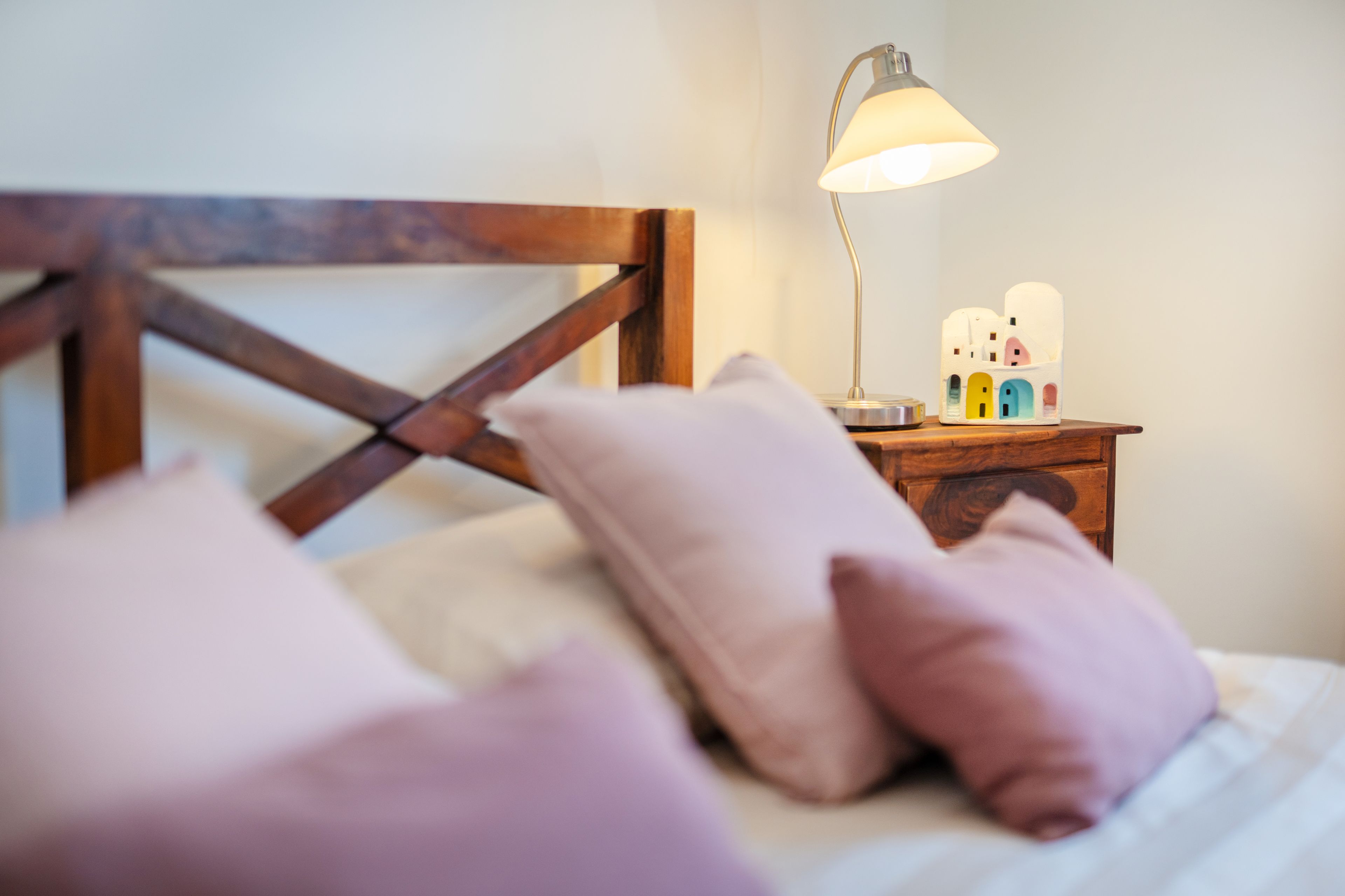 Ein Bett mit Holz-Kopfbrett, einer Nachttischlampe und zwei dekorativen Gegenständen auf dem Nachttisch.