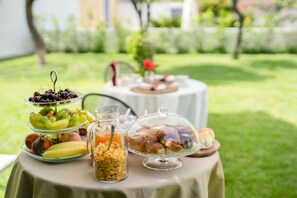 A table with a variety of food items including fruits, pastries, and a glass of juice, set outdoors on a sunny day. - Prochytea (Procida)