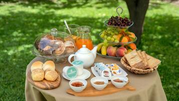 A picnic setup with food items, a teapot, and a fruit display on a table outdoors.