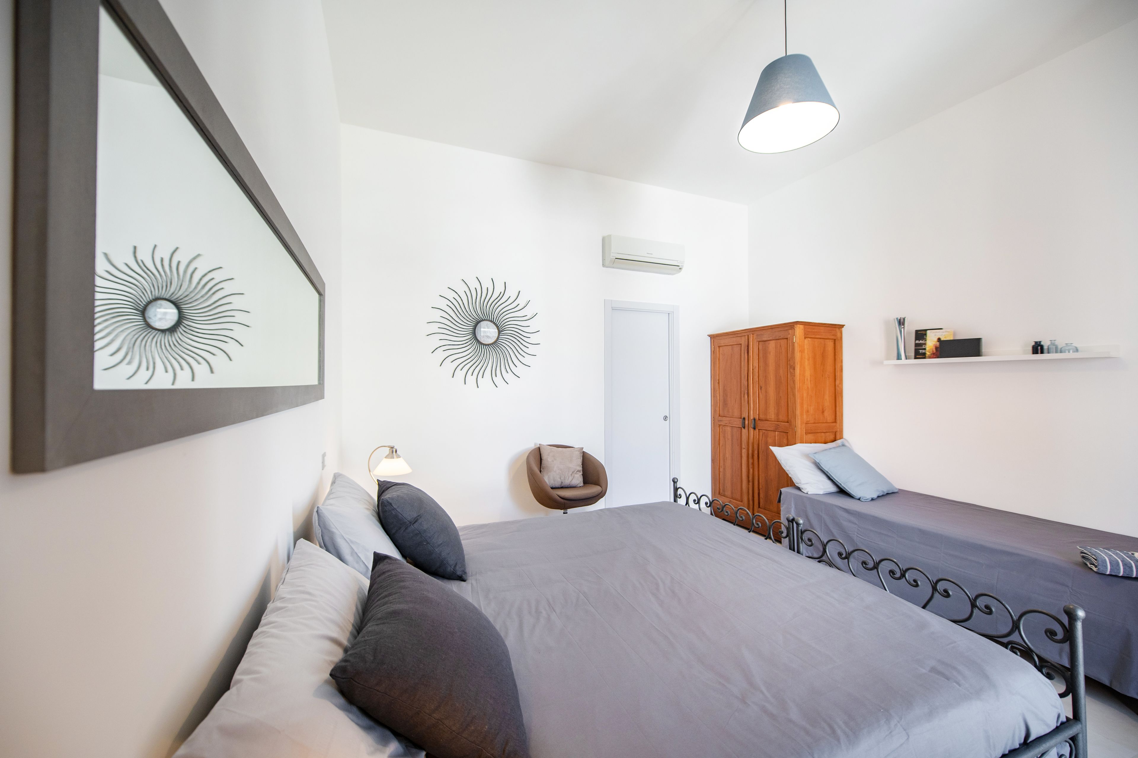 Quarto com duas camas, guarda-roupa de madeira, uma cadeira e decorações nas paredes.