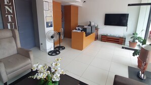 A modern living room with a sofa, a coffee table with flowers, a reception desk, and a TV mounted on the wall. - Hotel Zenturia (Boac)