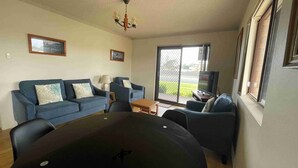A living room with a sofa set, a coffee table, a TV, and a large window. - Seabreeze 6 - Opposite Tuncurry Bowling Club! (Tuncurry)