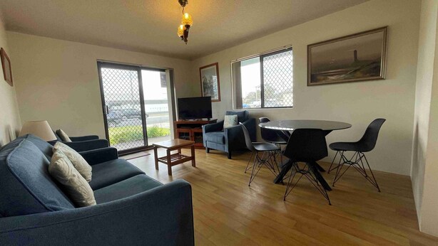 A living room with a sofa, a TV, a dining table with chairs, and large windows. - Seabreeze 6 - Opposite Tuncurry Bowling Club! (Tuncurry)