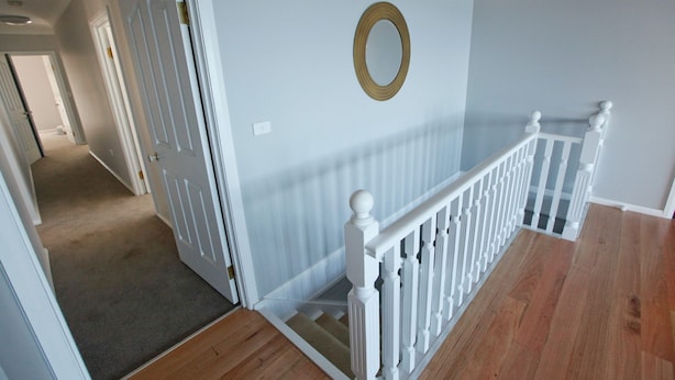 Eine Treppe mit weißen Balustraden und Holzboden, die zu einem Raum mit hellblauen Wänden und einem dekorativen Spiegel führt.