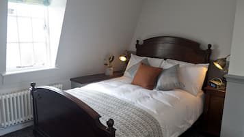 A neatly made bed with a wooden headboard, a bedside table with a lamp, and a window with curtains.