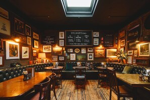 A cozy restaurant with wooden tables and booths, framed pictures on the walls, and a chalkboard menu.