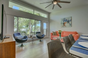 A spacious living area with a large window, a ceiling fan, a sofa, a dining table set, and a painting on the wall. - Lido Key Villa: Walk to Beach, Pool, St. Armands (Sarasota)