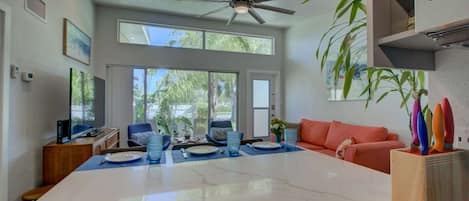 A modern kitchen with a large island, a ceiling fan, and a dining area with a red sofa and blue chairs.