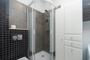 A modern bathroom with a glass-enclosed shower, a white cabinet with drawers, and a black tiled wall. - Apartament Wierzbowa Centrum (Poznan)