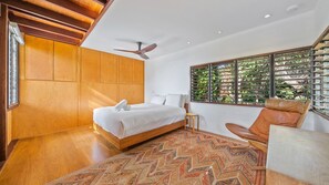 Une chambre à coucher avec un lit, un ventilateur de plafond, une fenêtre avec des stores et un tapis à motifs.