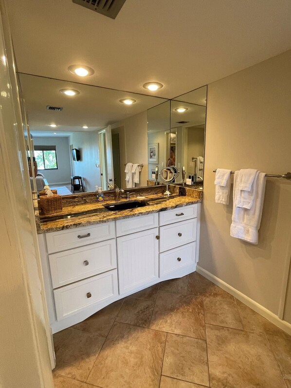 A modern bathroom with a granite countertop, white cabinetry, a large mirror, and a towel rack. - Updated 2 Bedroom, 2 Bath Gulf View with 2 Lanais! (Siesta Key)