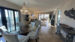Un salon spacieux avec une table à manger en verre, des sièges confortables, un lustre et un balcon offrant une vue imprenable.