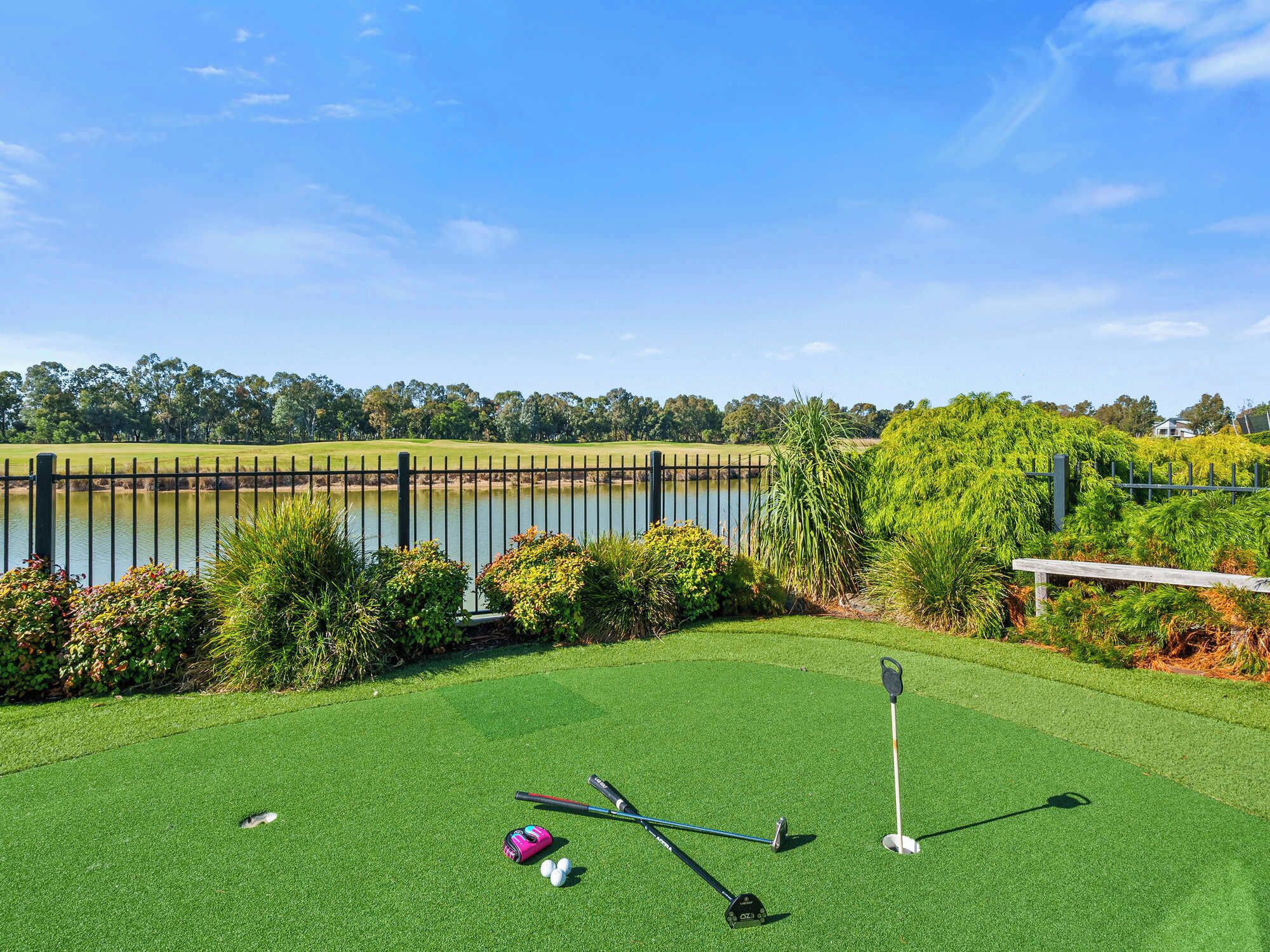 A golf course with a water body, a fence, and greenery.