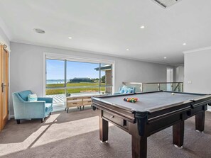 A pool table in a room with a large window, a blue armchair, and a view of a building and water.