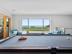 A pool table with balls, a sofa, and a large window with a view of the sea.