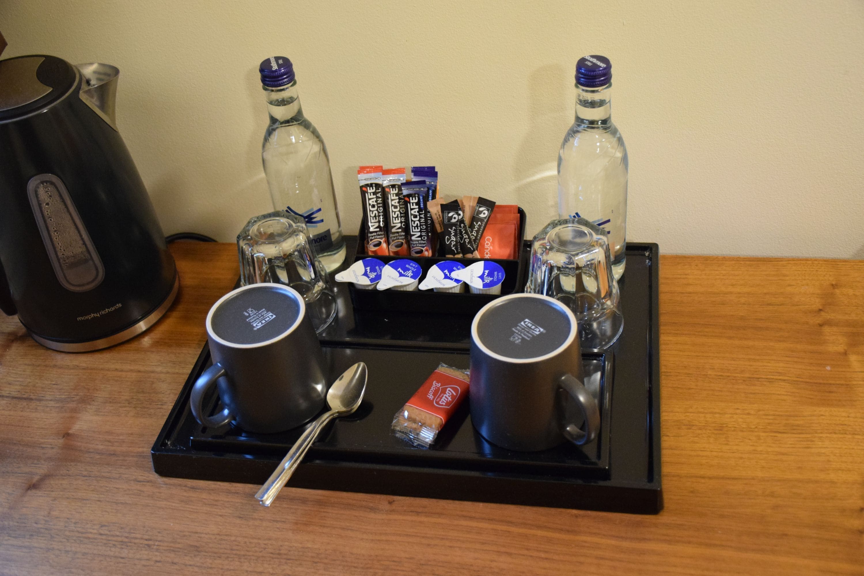A tray with two black mugs, a spoon, a box of Nespresso capsules, and two clear bottles.
