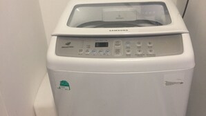 A Samsung washing machine in a small laundry room with a purple basket on the wall and two detergent bottles on the floor. - Friendly host looking for polite guests (Tp. Vũng Tàu)