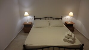 Una cama individual con estructura metálica, dos mesitas de noche con lámparas y una toalla doblada con cuidado sobre la cama.