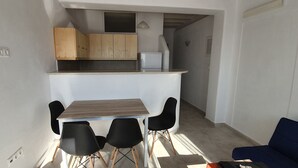 Un espacio habitable compacto con kitchenette, una zona de comedor con mesa y sillas, y un sofá azul.