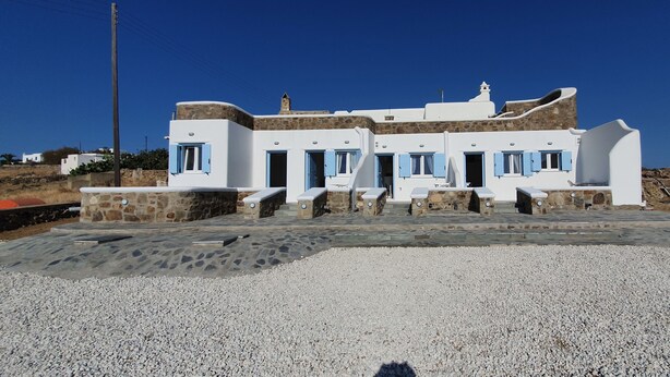 Un edificio blanco con contraventanas azules, detalles de piedra y un camino de entrada de grava.