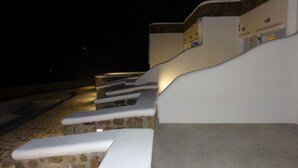 Vista nocturna de un edificio con escalones de piedra y barandillas blancas, iluminado por luces artificiales.