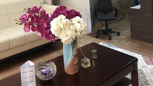 A reception area with a sofa, a desk with a vase of flowers, a bookshelf, and a mural of a person on a beach. - Hotel Sirdaria (Kyzylorda)