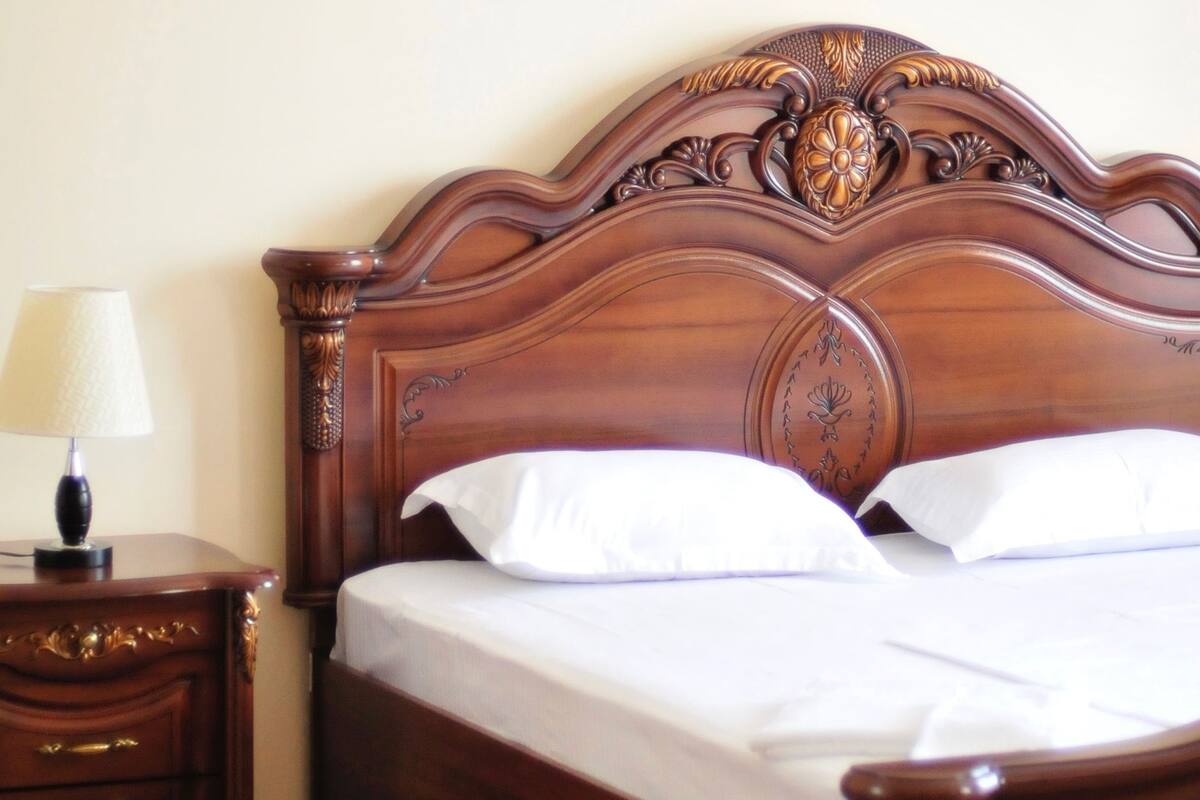 Una cama de madera con cabecera, una mesita de noche con lámpara y una alfombra estampada.