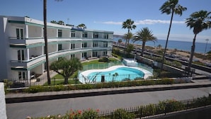A hotel with a pool, palm trees, and a view of the sea. - Apartamentos Arco Iris (San Bartolomé de Tirajana)