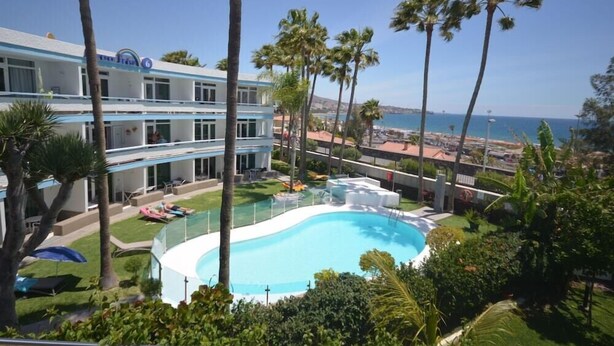 A hotel with a swimming pool, palm trees, and a view of the ocean. - Apartamentos Arco Iris (San Bartolomé de Tirajana)