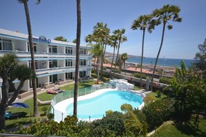 Un hotel con piscina, palmeras y vistas al océano.