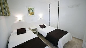 A hotel room with two single beds, a small bedside table, a nightstand, a wardrobe, and a framed picture on the wall. - Apartamentos Arco Iris (San Bartolomé de Tirajana)