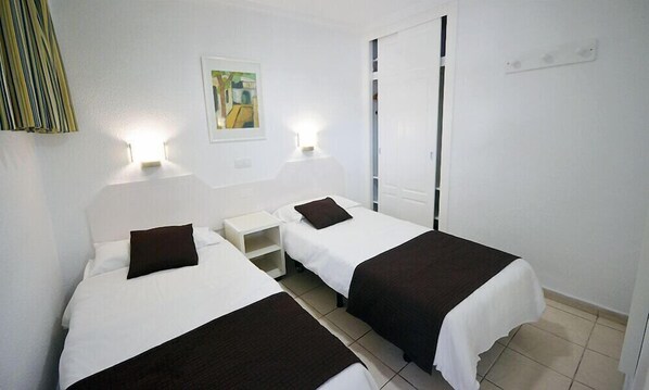 Habitación de hotel con dos camas individuales, una mesita de noche, un armario y un cuadro en la pared.