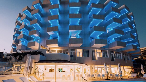Un hotel moderno con una fachada geométrica singular, un área de piscina con tumbonas y un bar o sala de estar.