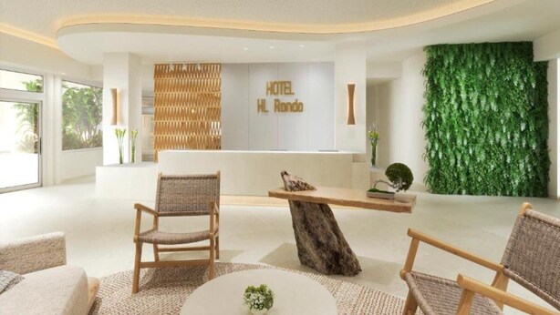 A modern hotel lobby with a reception desk, wicker chairs, and a green vertical garden. - HL Hotel Rondo (San Bartolomé de Tirajana)