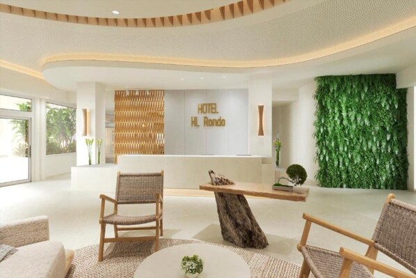 A modern hotel lobby with a reception desk, wicker chairs, and a green vertical garden. - HL Hotel Rondo (San Bartolomé de Tirajana)