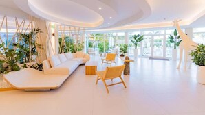 Un amplio y moderno salón con un sofá blanco, sillas de mimbre y una gran estatua de jirafa.