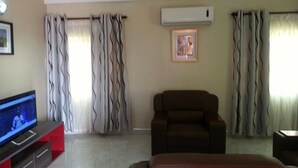 A living room with a flat-screen TV, a brown leather sofa, and a red entertainment unit. - MJ Appartments (Accra)