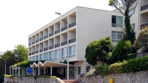A modern hotel with a multi-story structure, a covered entrance, and a stone retaining wall with greenery. - Adriatica Rooms (Dubrovnik)