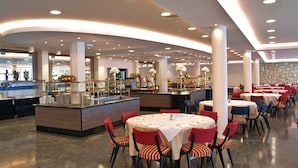 A spacious hotel dining area with round tables, red and blue chairs, and a central island with a buffet. - Adriatica Rooms (Dubrovnik)