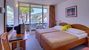 A hotel room with two beds, a desk, and a balcony with a view of the sea and hills. - Adriatica Rooms (Dubrovnik)